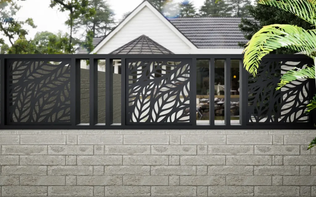 Cerco de paneles decorativos de chapa con hojas sobre un muro, frente a una casa