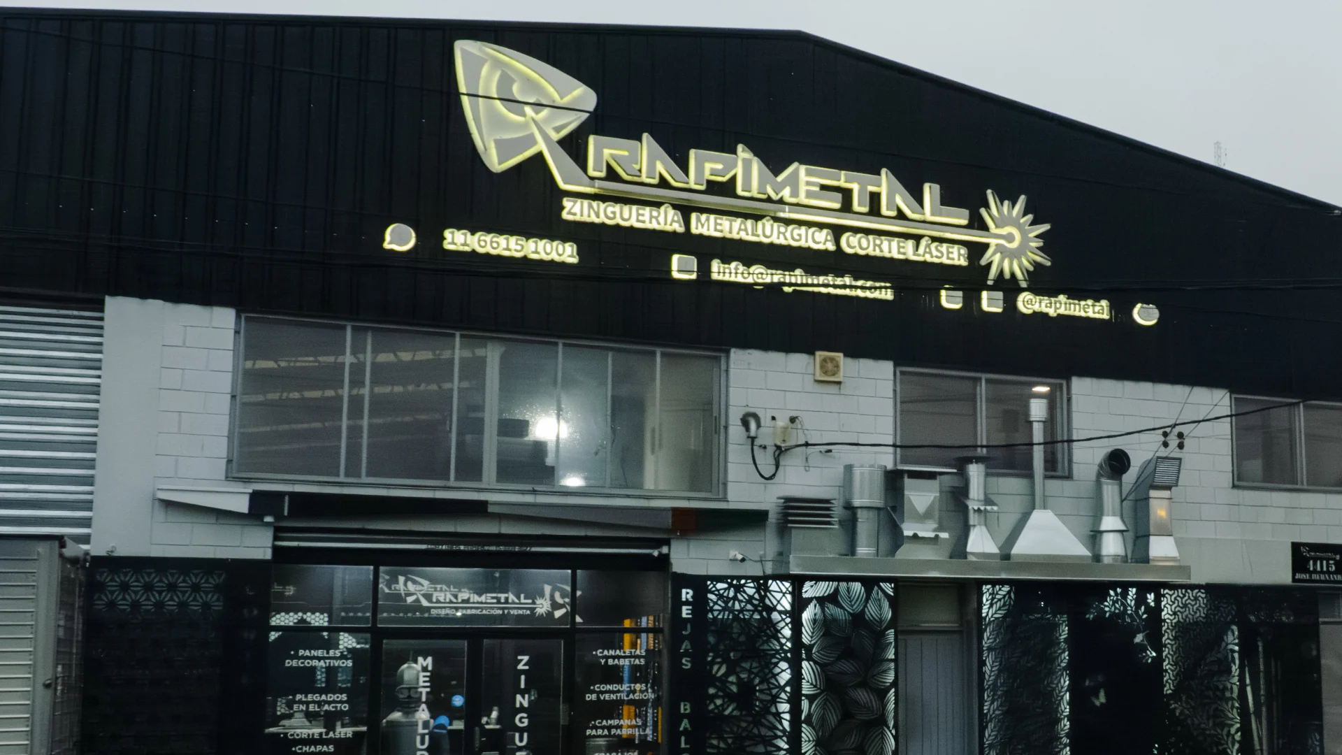Frente del local y planta de Rapimetal en Villa Ballester al atardecer, con el cartel encendido